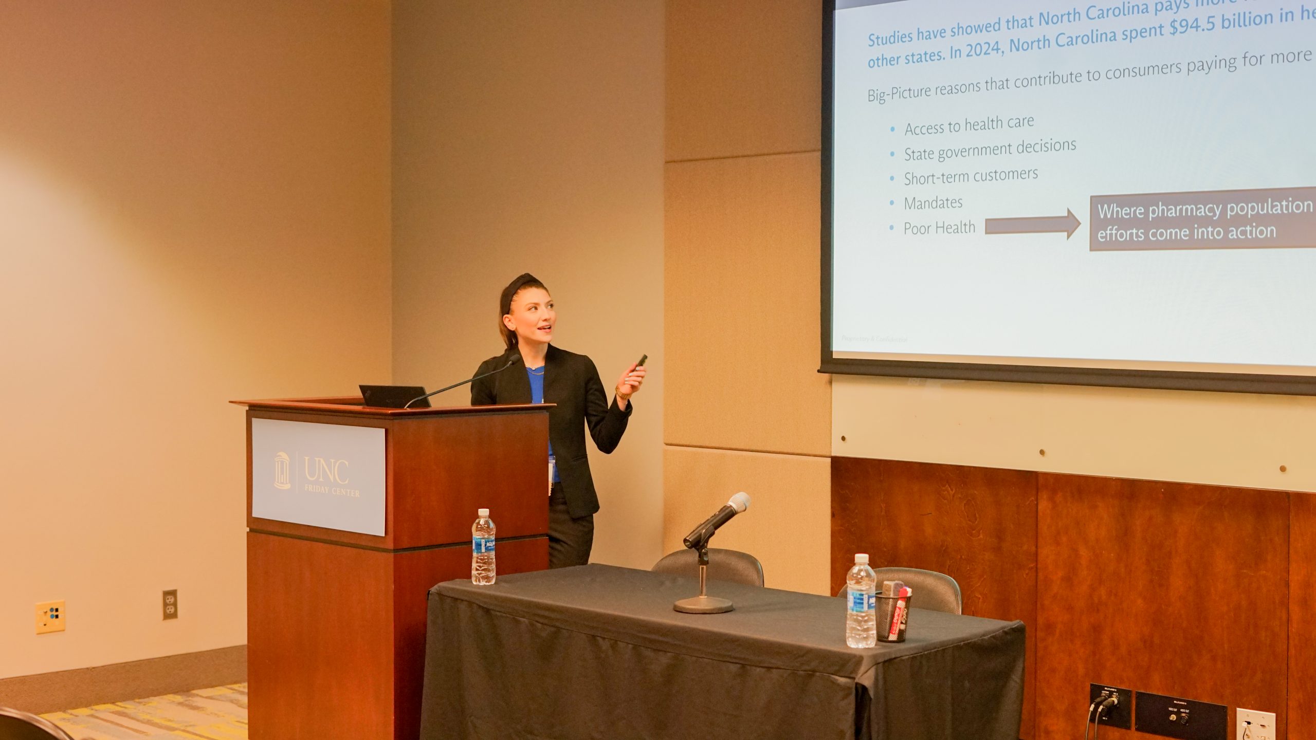 Female alumna presenting at podium holding a slide advance clicker.