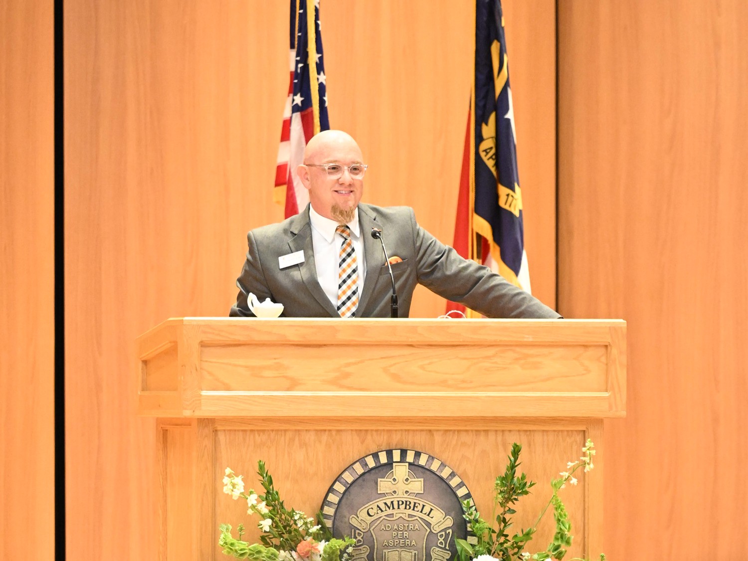 Male wearing suit and striped tie speaking at podium.