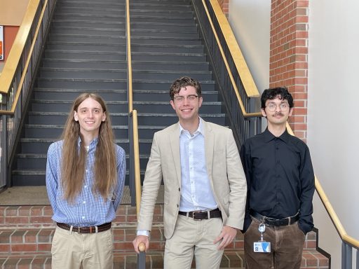 Three male students standing at the base of a staircase.