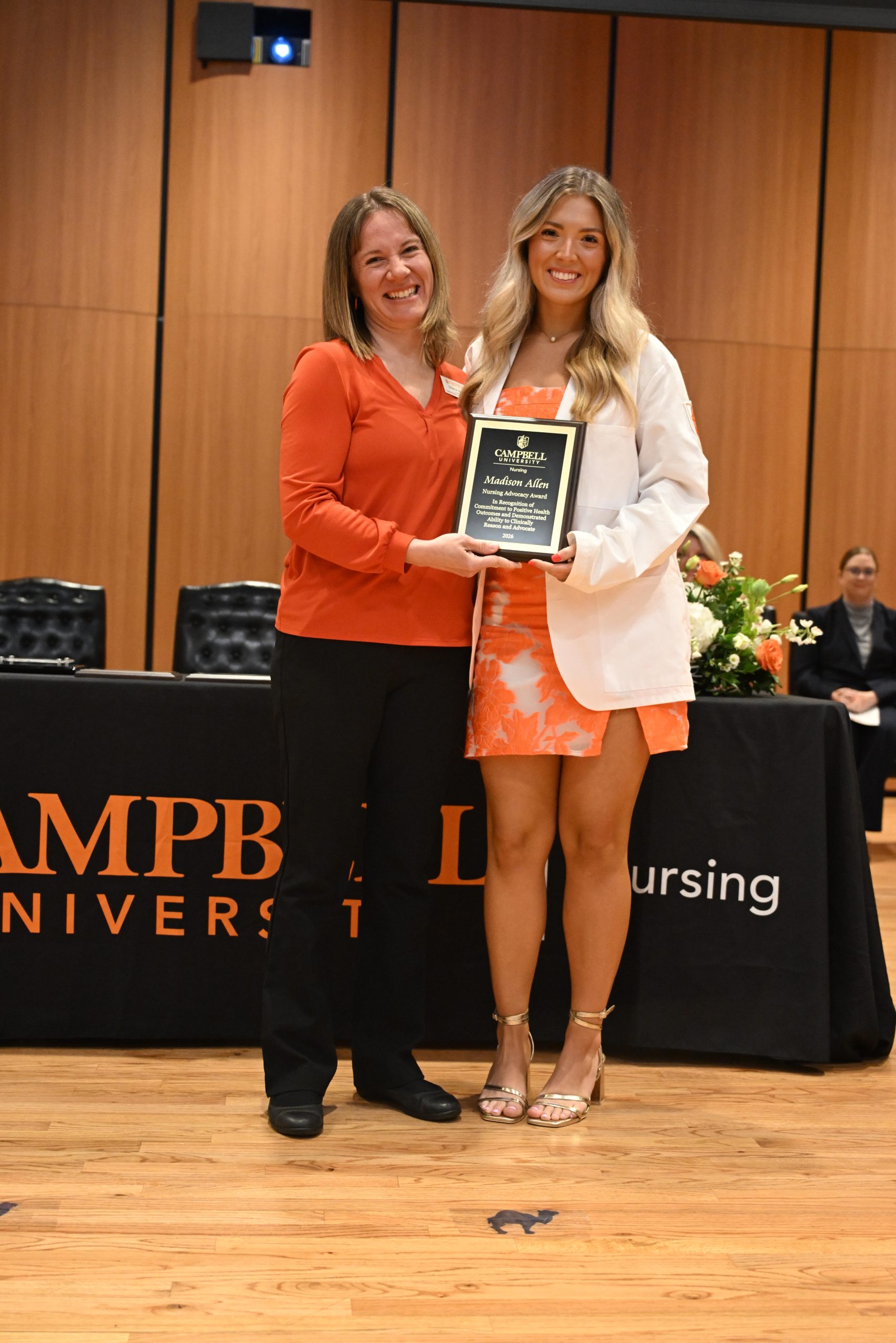 Female faculty member stands with female student holding plaque.
