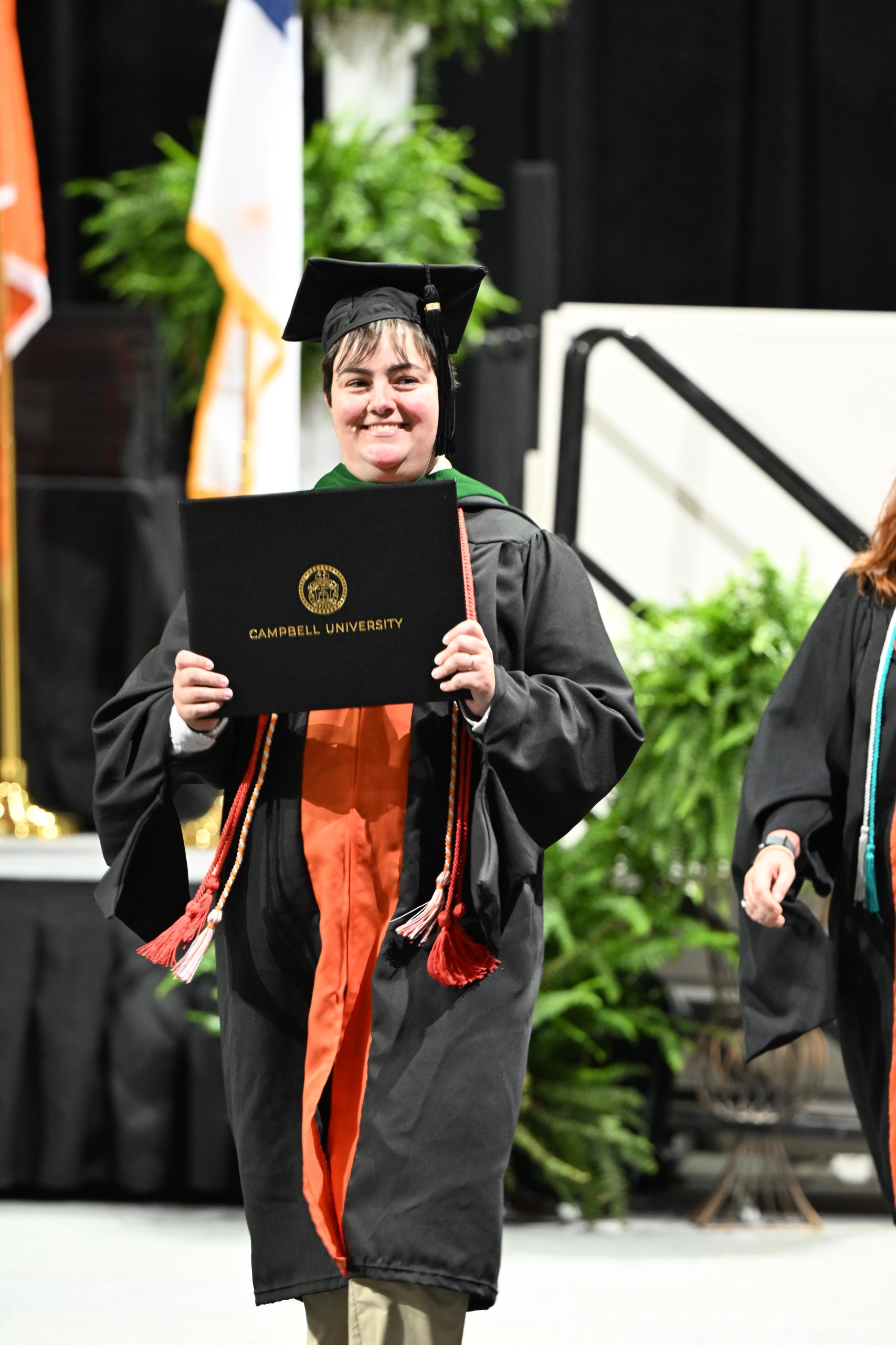 Female studnet walking off stage with big smile holding diploma folder.