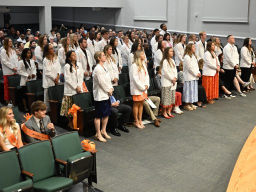 Nursing students wearing white coats standing in rows.