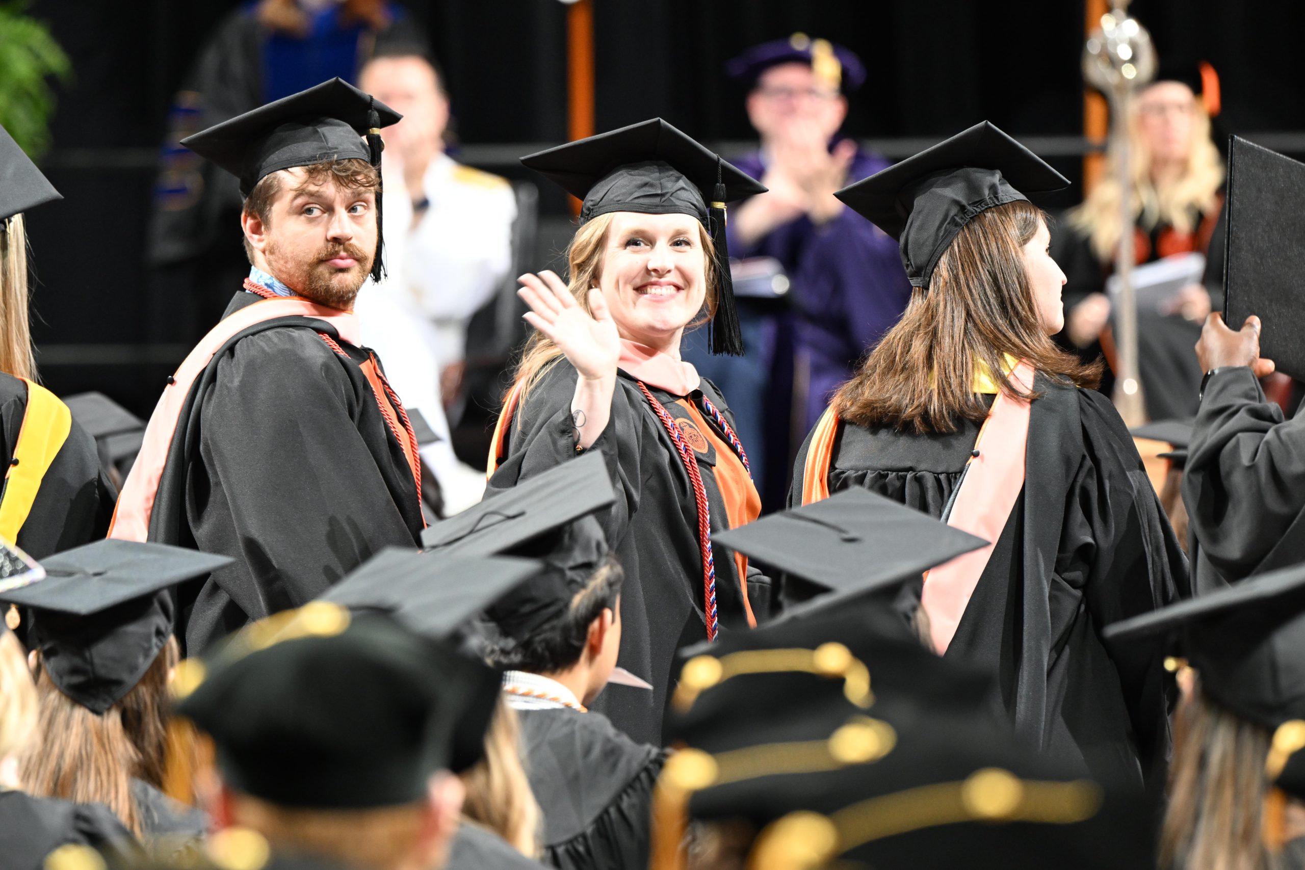 Female student turning to look over shoulder and wave while sitting in rows
