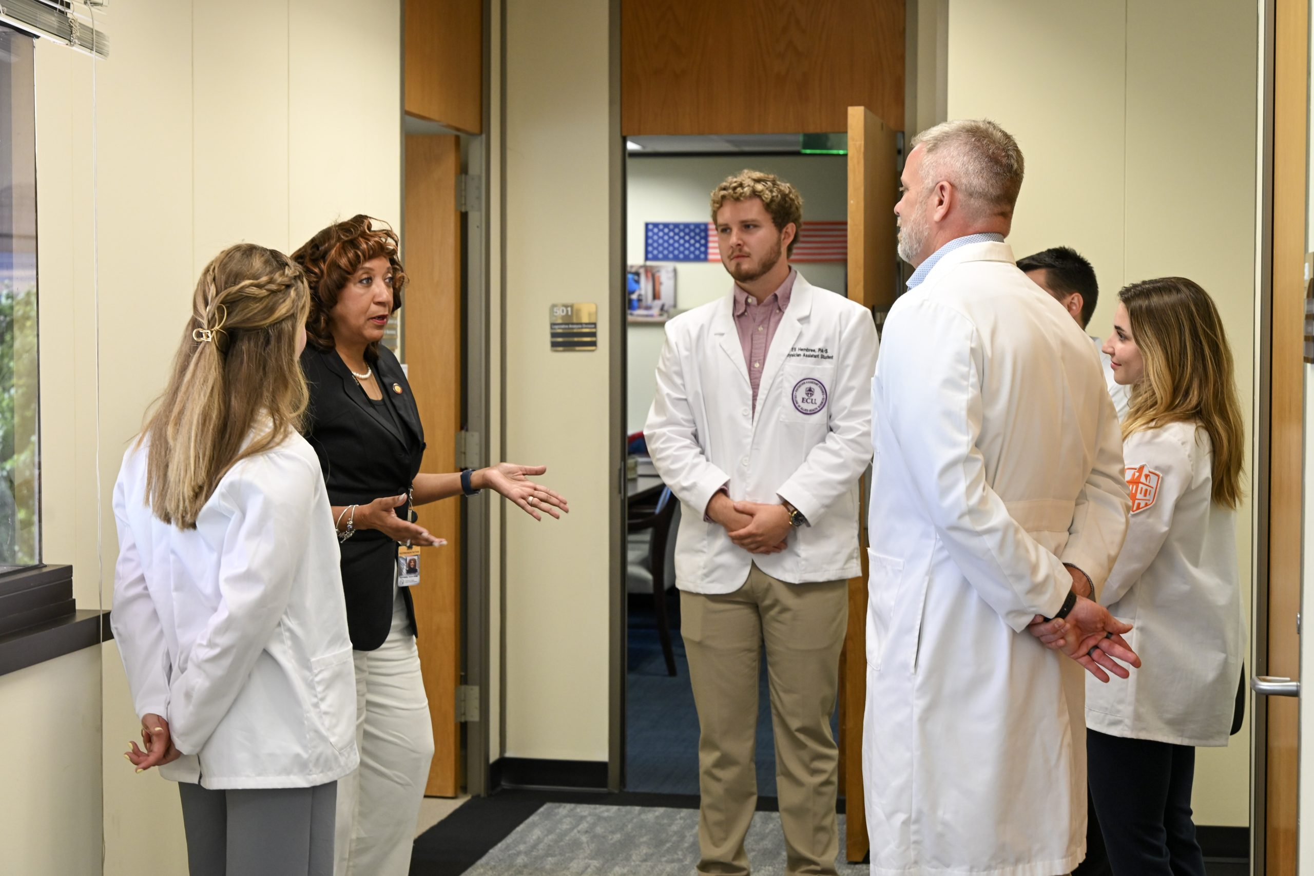 PAs in white coats talk with a female member of the legislature.