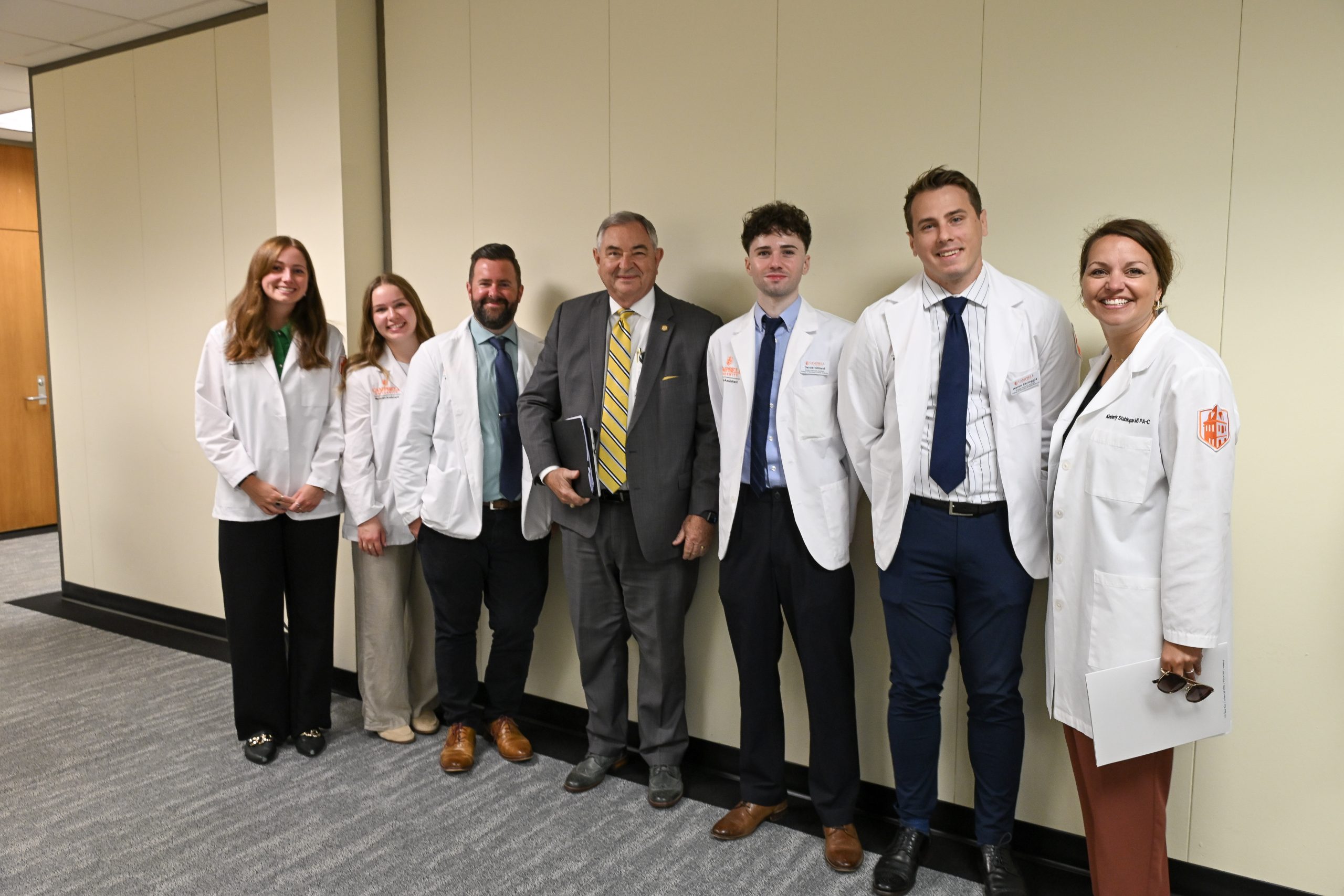 male and female students in white coats stand with North Carolina Sen. Jim Burgin
