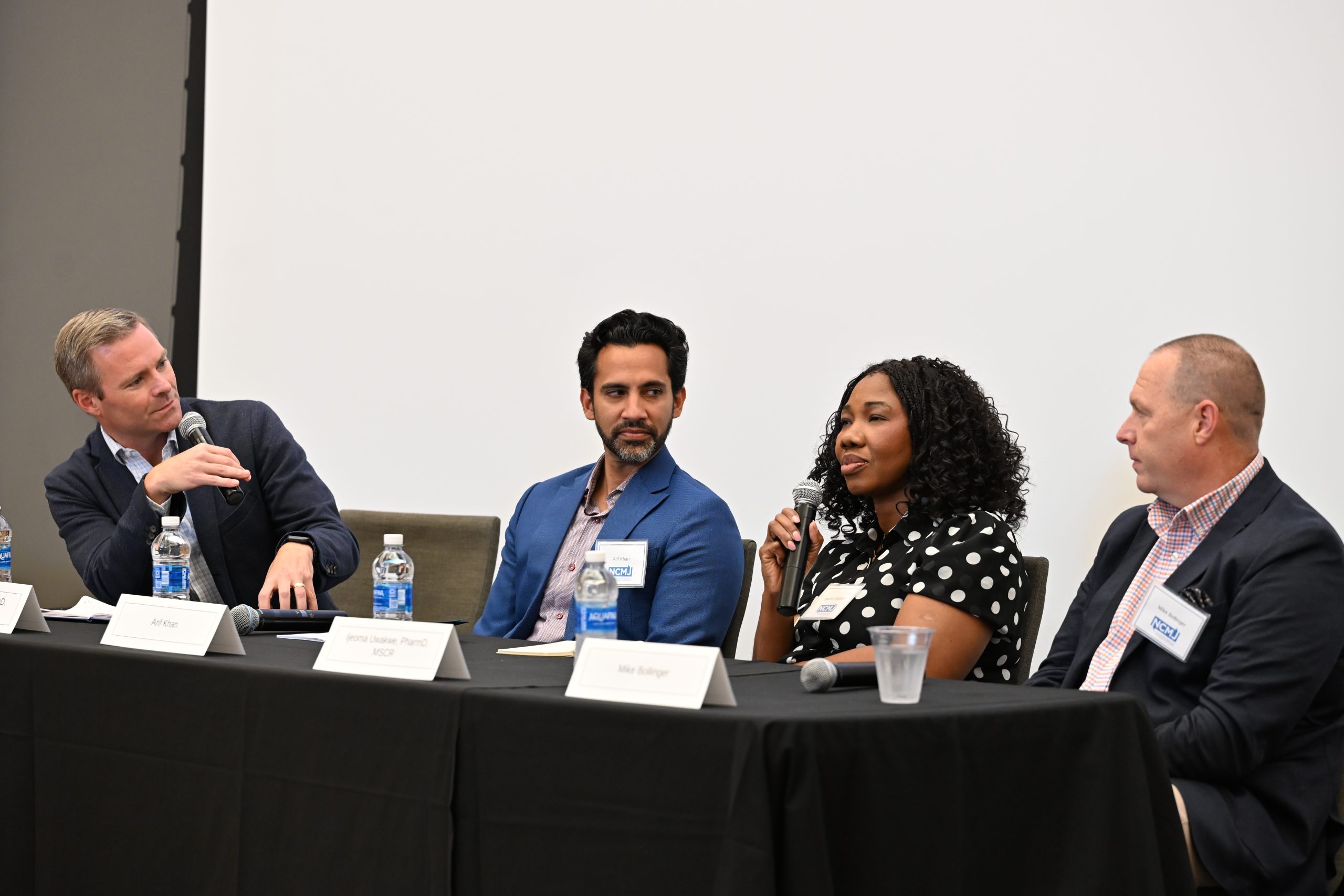 Three male panelists and a female panelist sitting at the head table on stage.