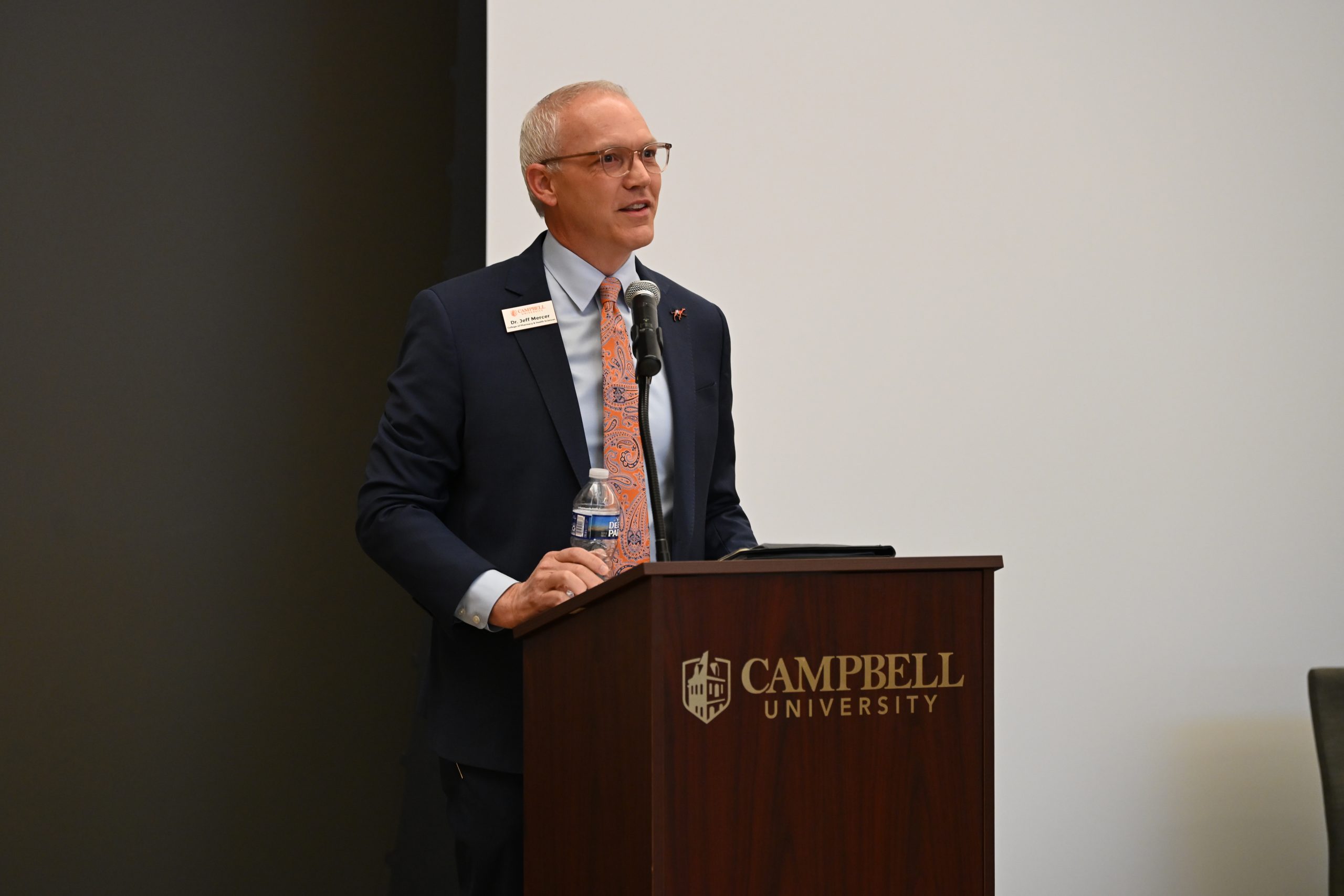 Dr. Jeff Mercer, dean of CPHS, welcoming attendees to the event standing at the podium wearing a business suit.