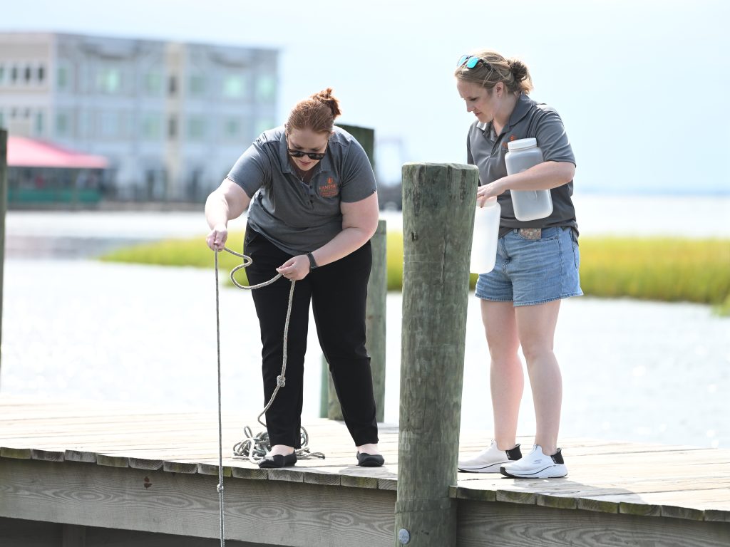 Two females on a pier collecting water samples.