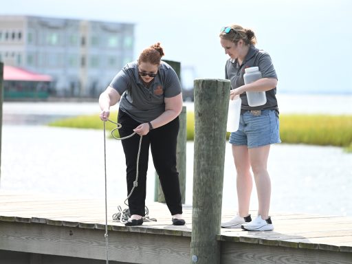 Two females on a pier collecting water samples.