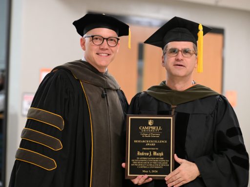 Two men wearing academic regalia standing together with one holding an award plaque.
