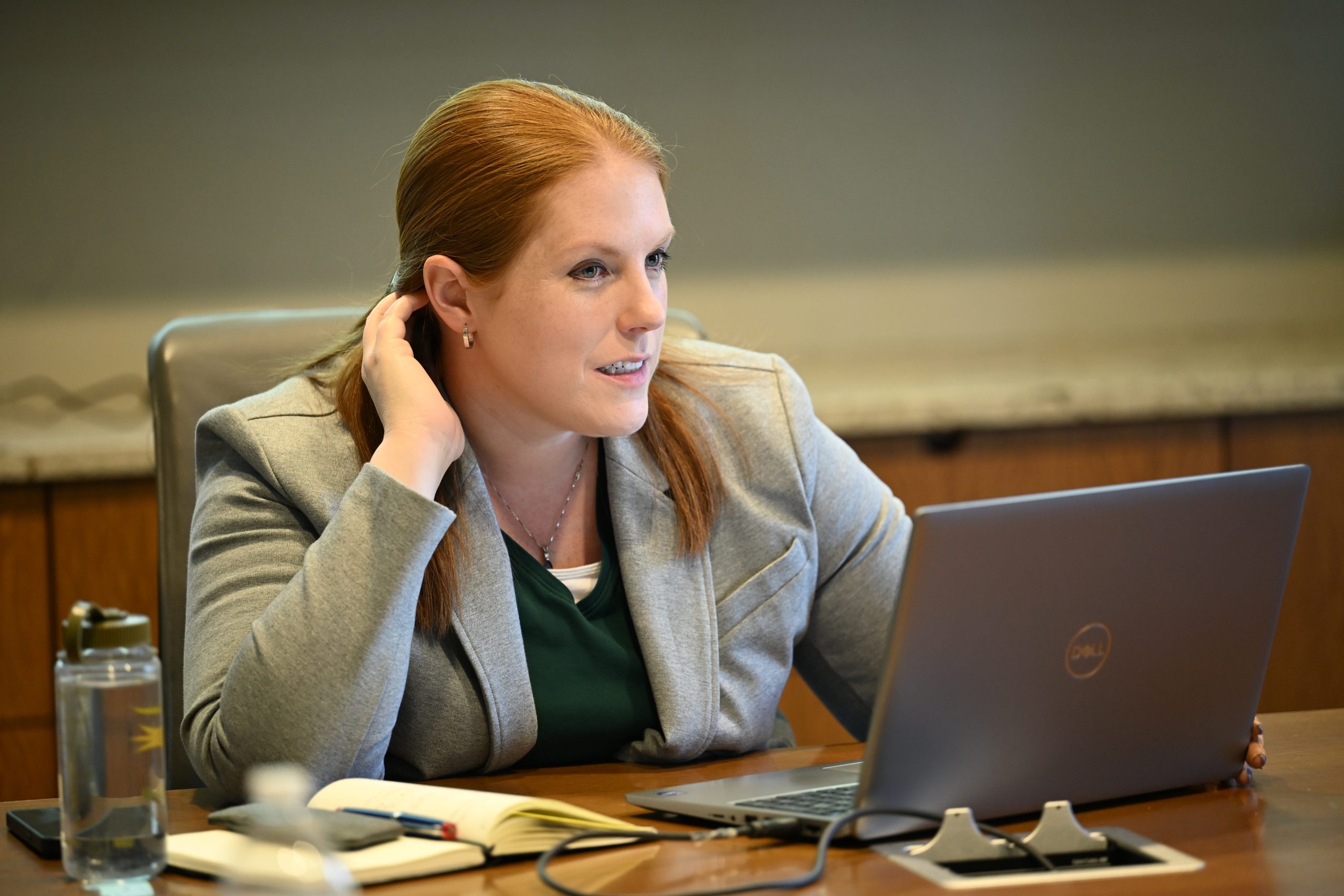 Female in grey blazer sitting at a laptop looks up across the table