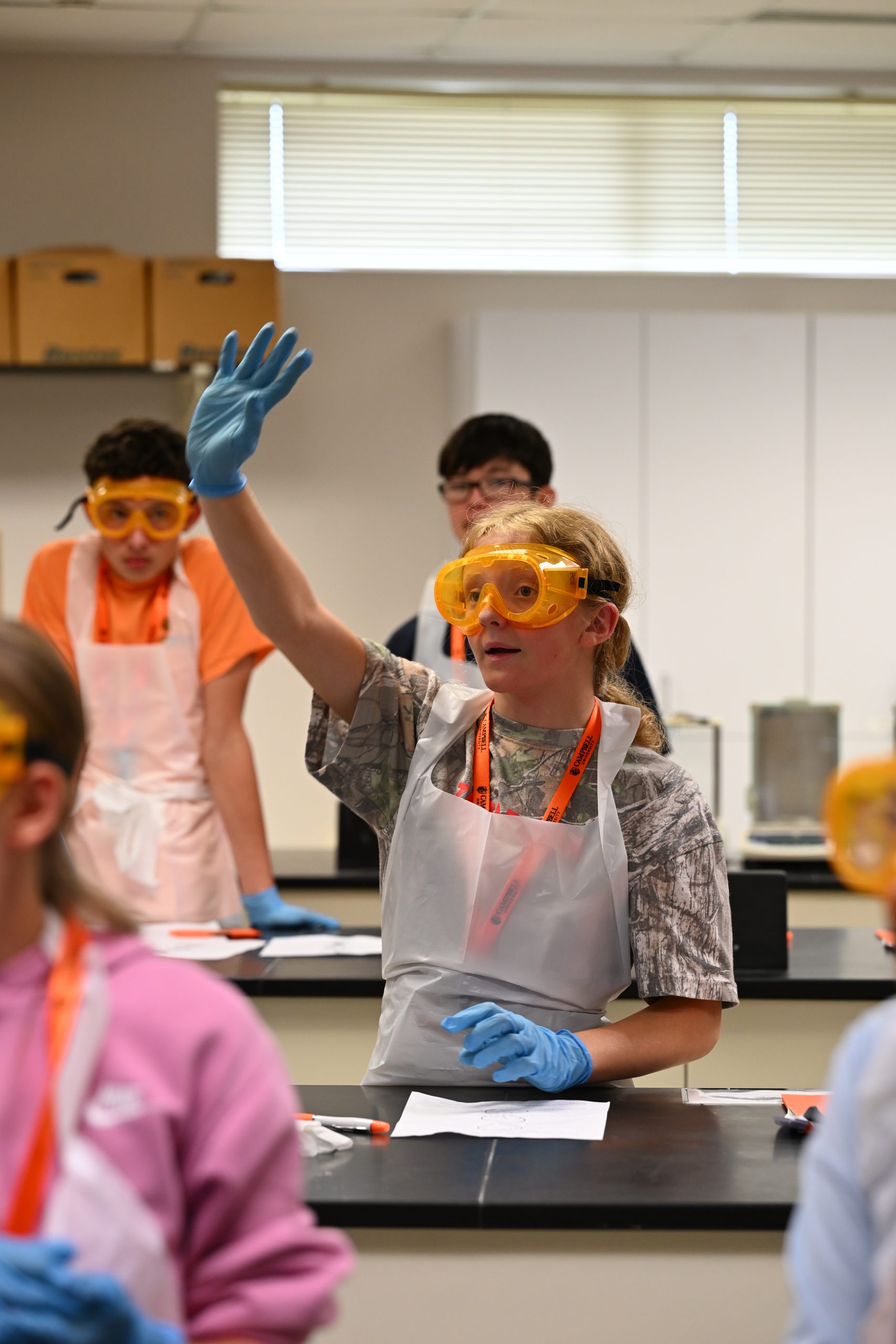 Female student wearing PPE in a lab raises hand