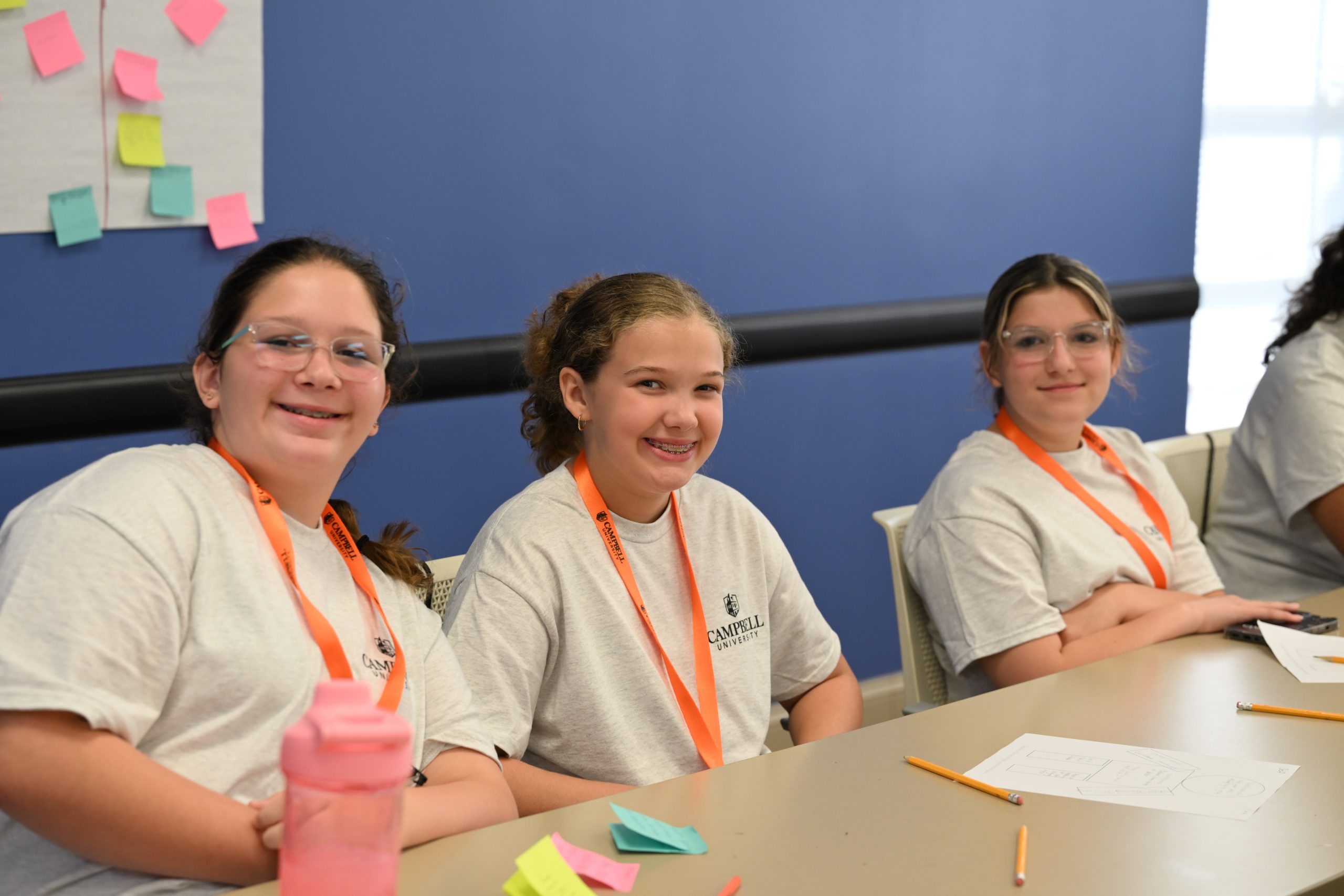 Three middle school STEM Camp participants smile during a collaborative classroom activity at Campbell University.