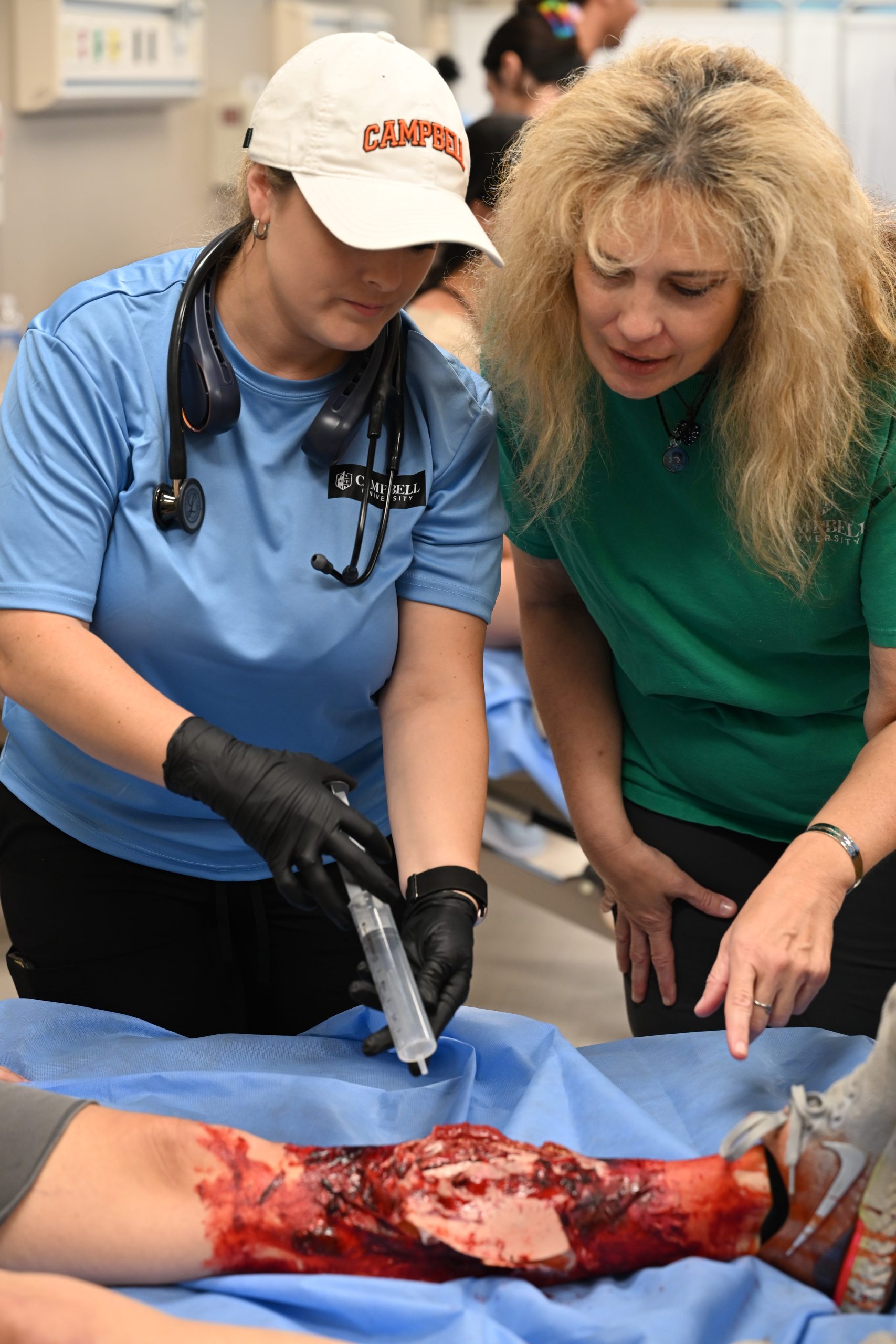 Female nursing professor points to injury to instruct female PA student on irrigating the injury