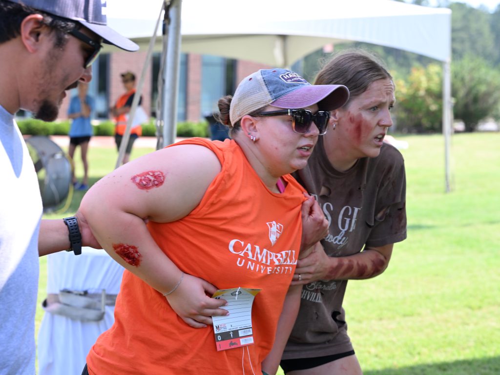 Two female participants with make up to look injured being helped by a male participant to a triage tent