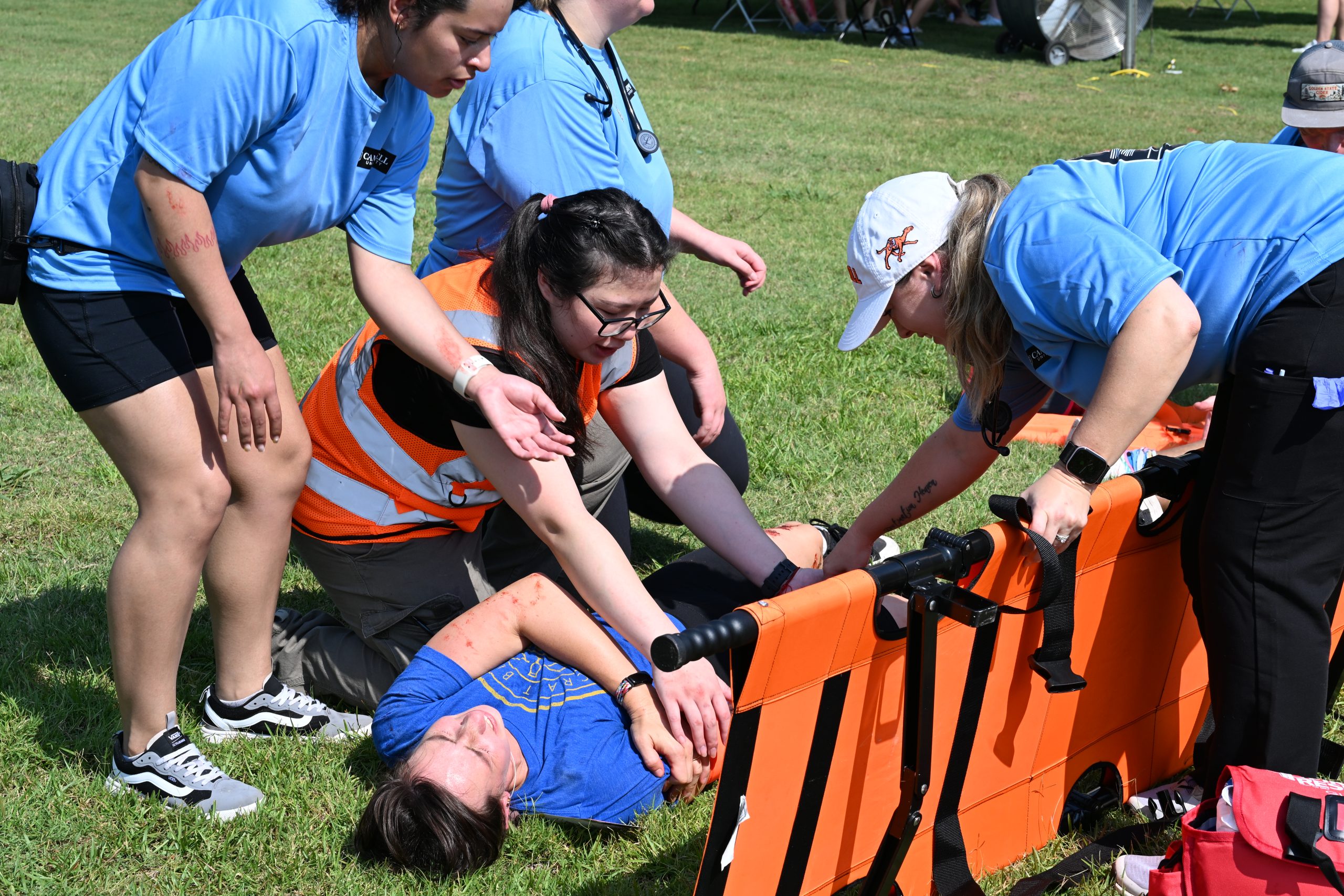 Female PA students working with a first responder to put an injured female patient on to a litter