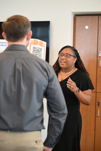 A woman presents her research poster while speaking with an attendee during a poster session at the Campbell University College of Pharmacy & Health Sciences.