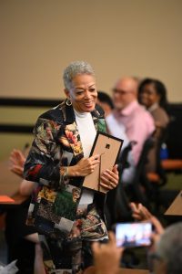 An attendee smiles while carrying a framed award through the audience during a recognition ceremony at the Campbell University College of Pharmacy & Health Sciences.