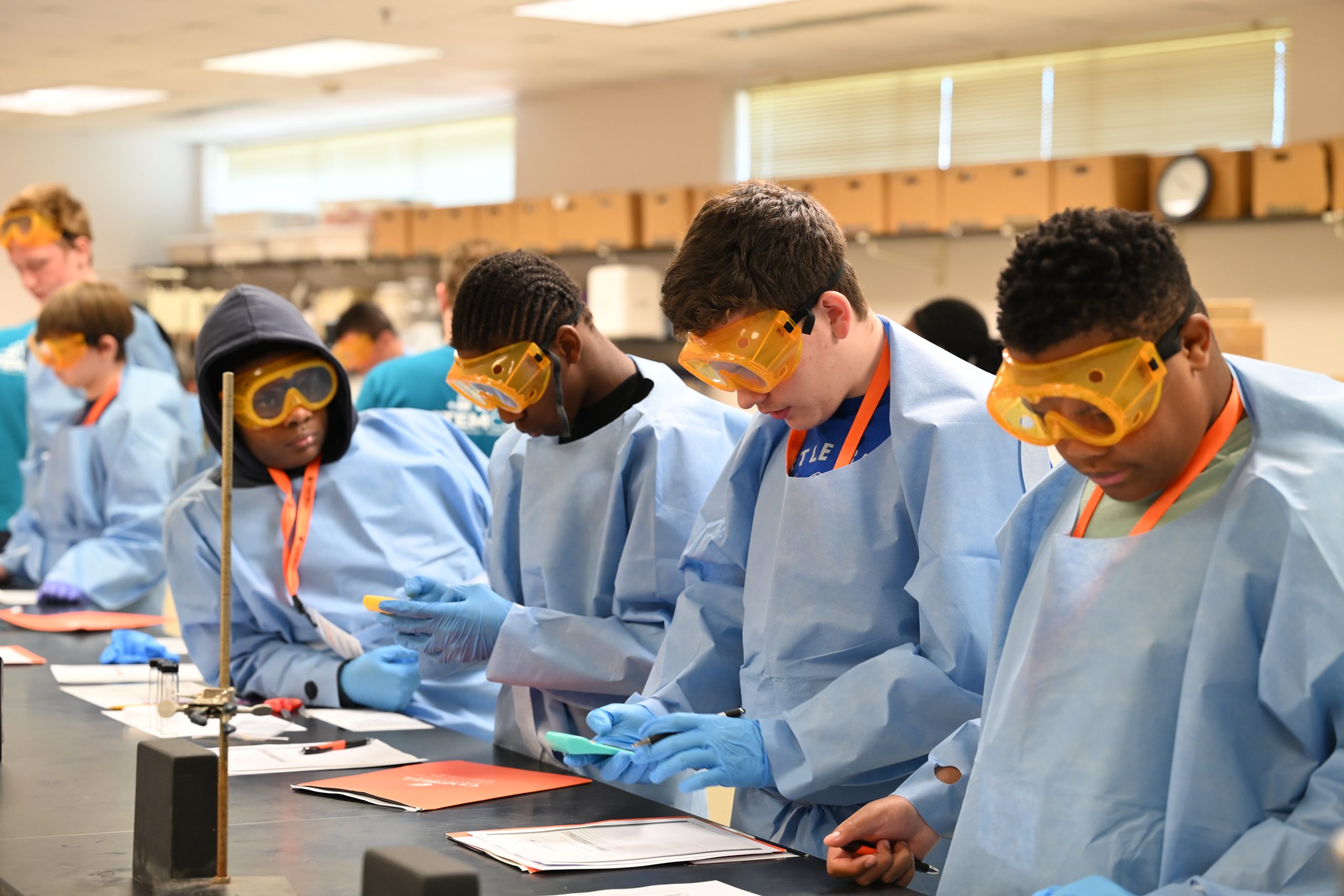 Students wearing protective lab equipment work together during a hands-on laboratory investigation.
