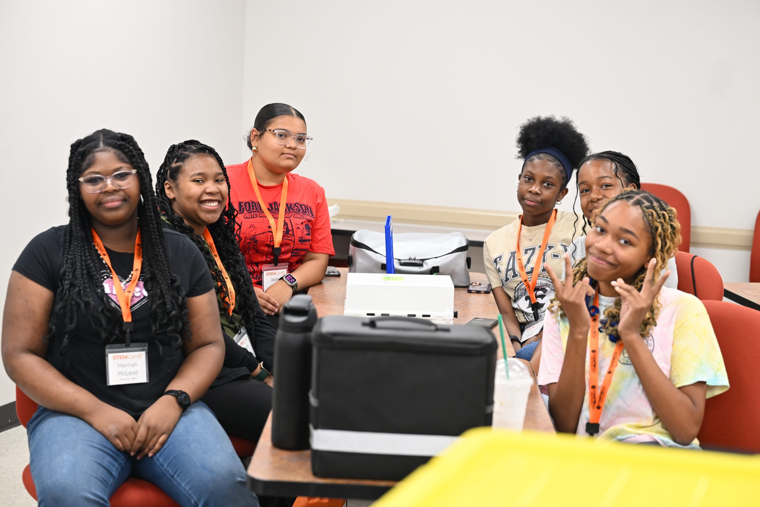 Four high school STEM Camp participants smile at the camera while seated together before beginning a classroom activity.