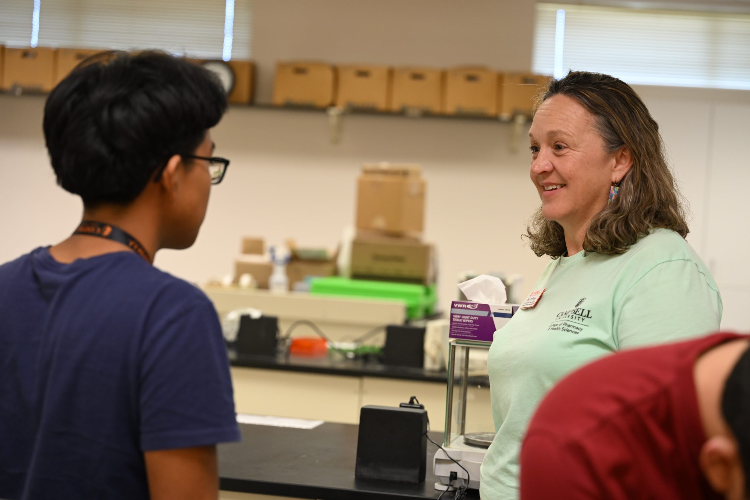 Faculty member smiles while speaking one-on-one with a student in a pharmaceutical sciences laboratory during a hands-on learning activity.