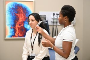 A student practices using a tuning fork to assess hearing during a clinical examination skills session with a classmate.