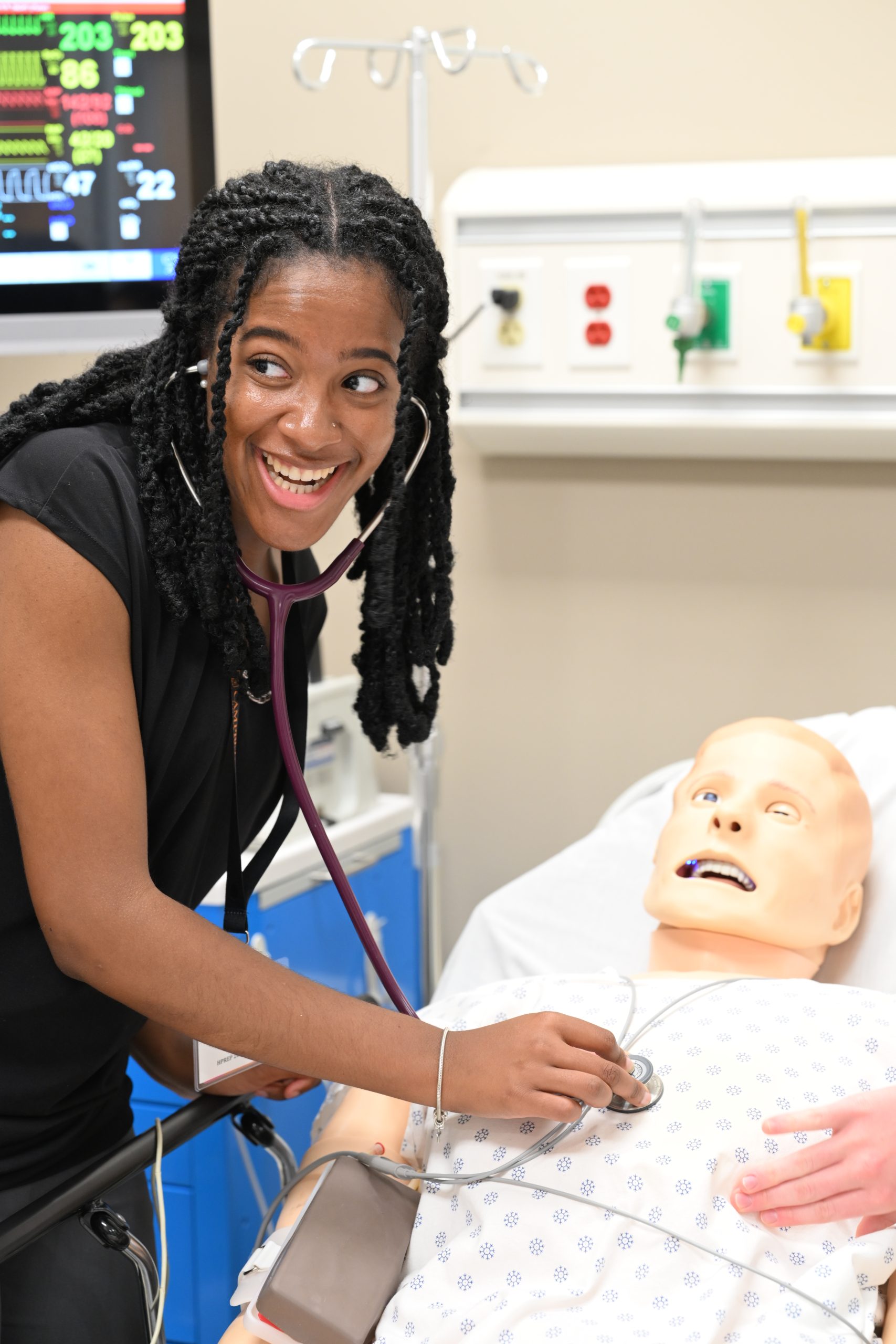 A student listens to a simulation mannequin's heart and lung sounds with a stethoscope during a clinical skills exercise.
