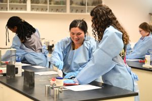 Students wearing lab gowns and gloves collaborate on a hands-on pharmaceutical sciences activity in a Campbell University laboratory.