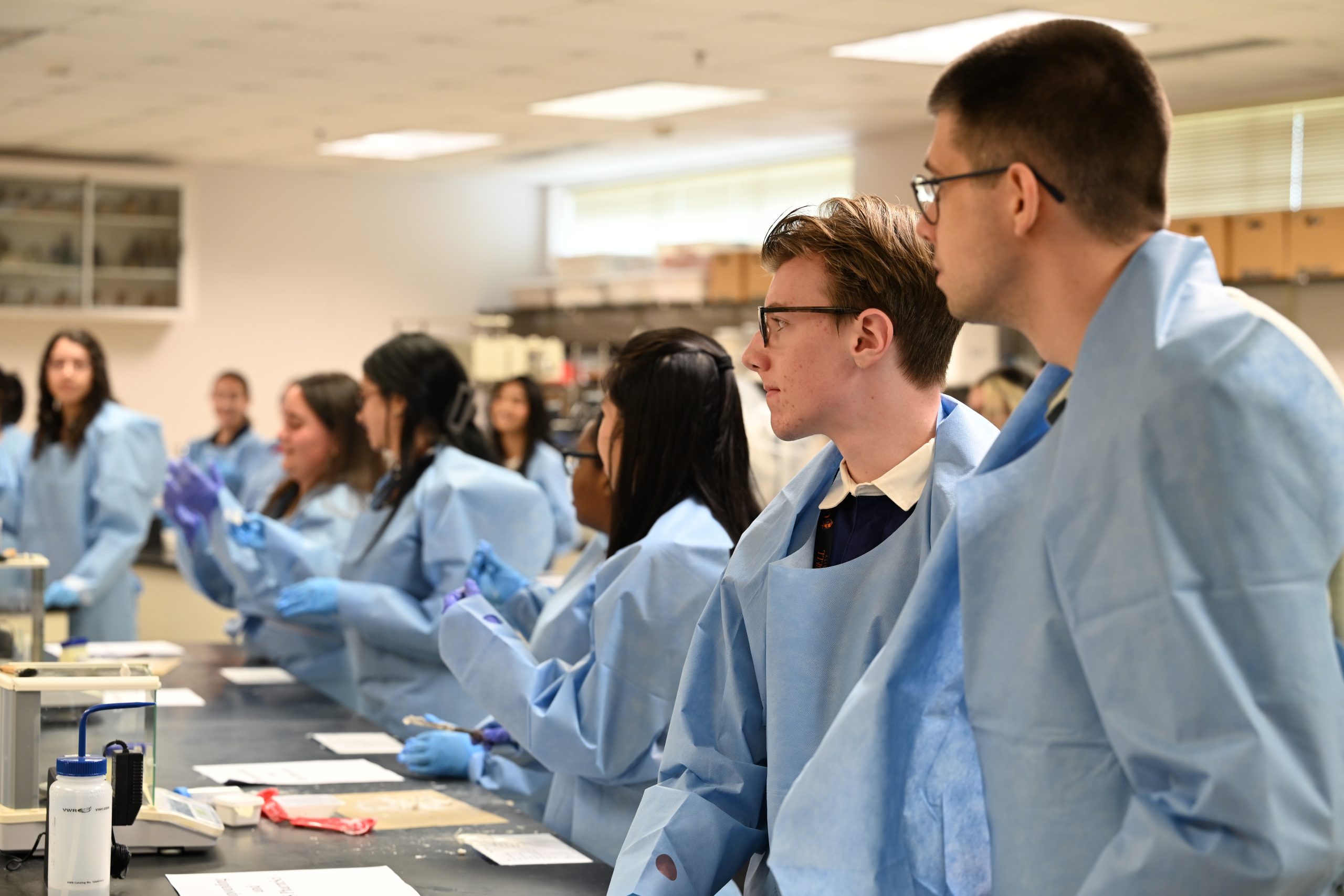 Students in protective lab gowns listen to instructions before participating in a hands-on laboratory exercise at Campbell University.