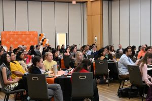 Students, faculty and guests listen attentively during a Campbell University College of Pharmacy & Health Sciences event in a banquet-style meeting room.