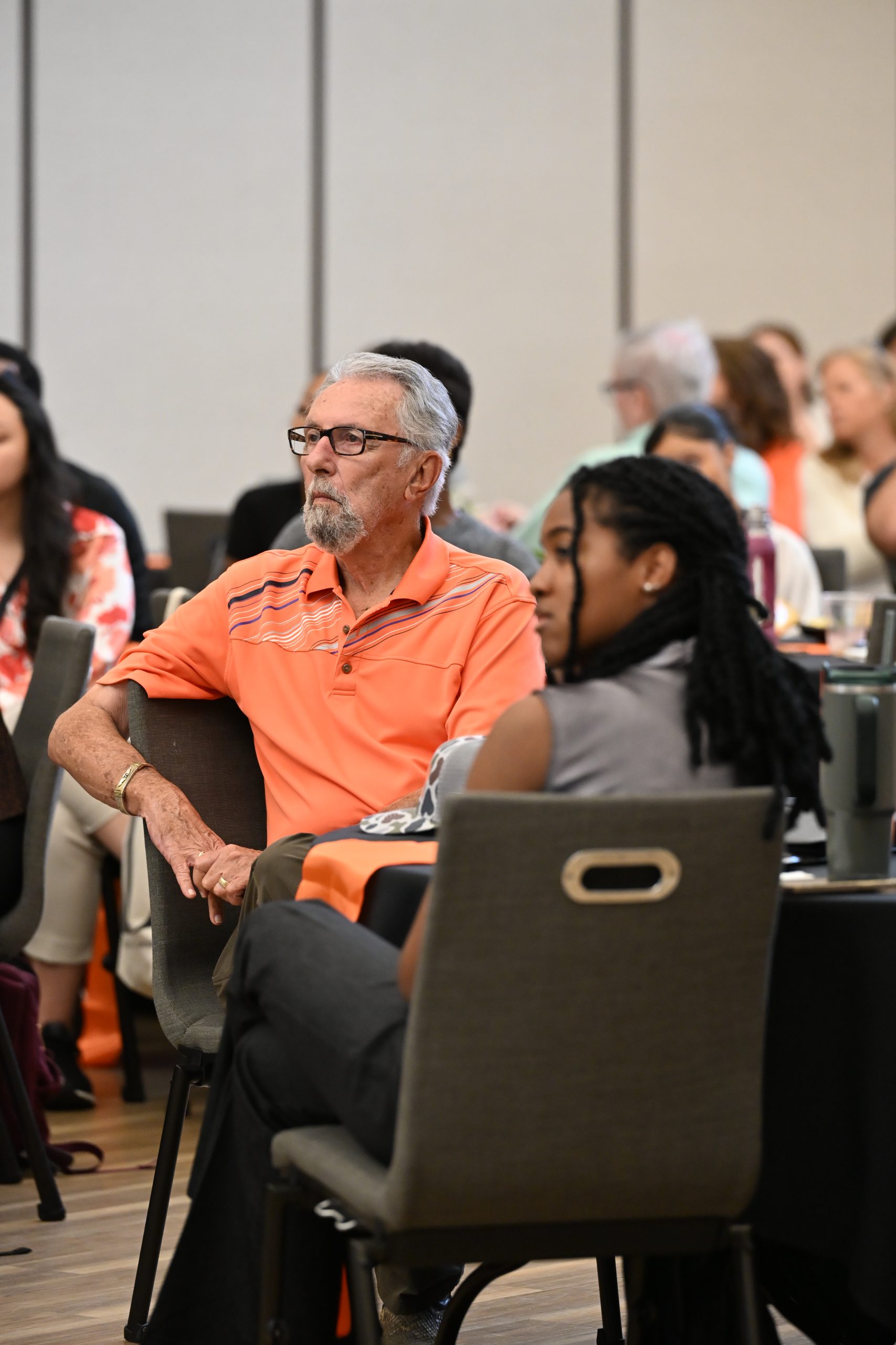 An attendee listens to a speaker during a Campbell University College of Pharmacy & Health Sciences event while seated among students and guests.