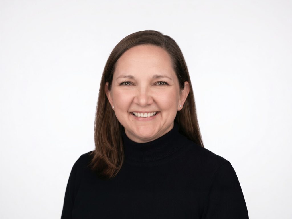 Professional headshot of Erin Kunz smiling at the camera while wearing a black turtleneck against a light gray background.