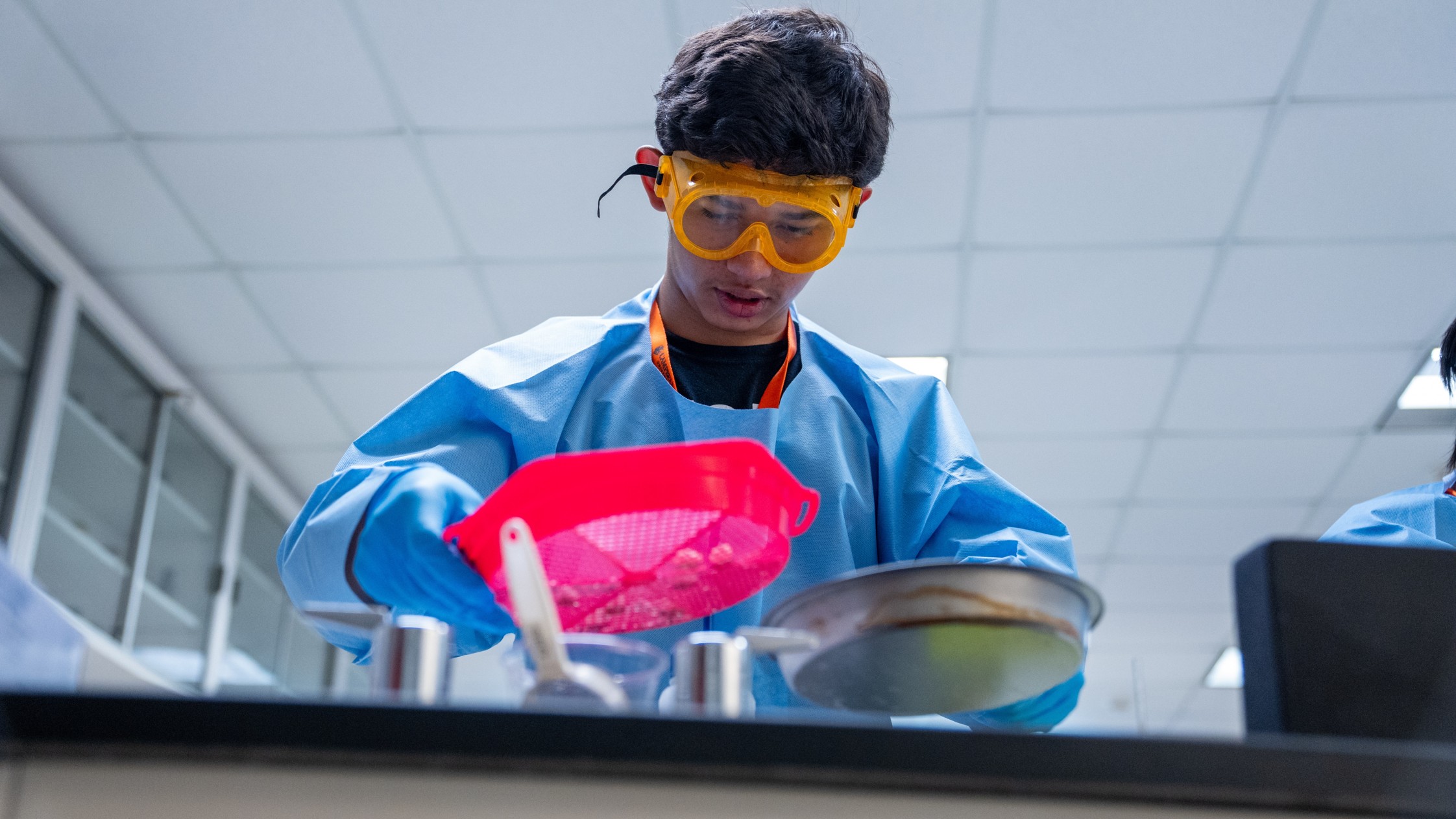 A student focuses on completing a laboratory activity while wearing safety goggles and protective gear.