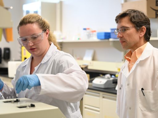 Faculty member watches as student uses equipment in science lab