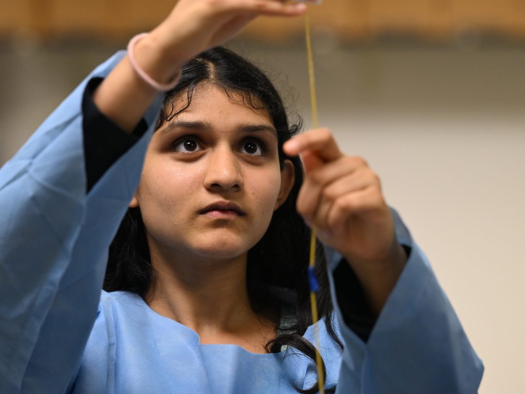 Student wearing PPE putting marshmallow on a piece of spaghetti during tower challenge