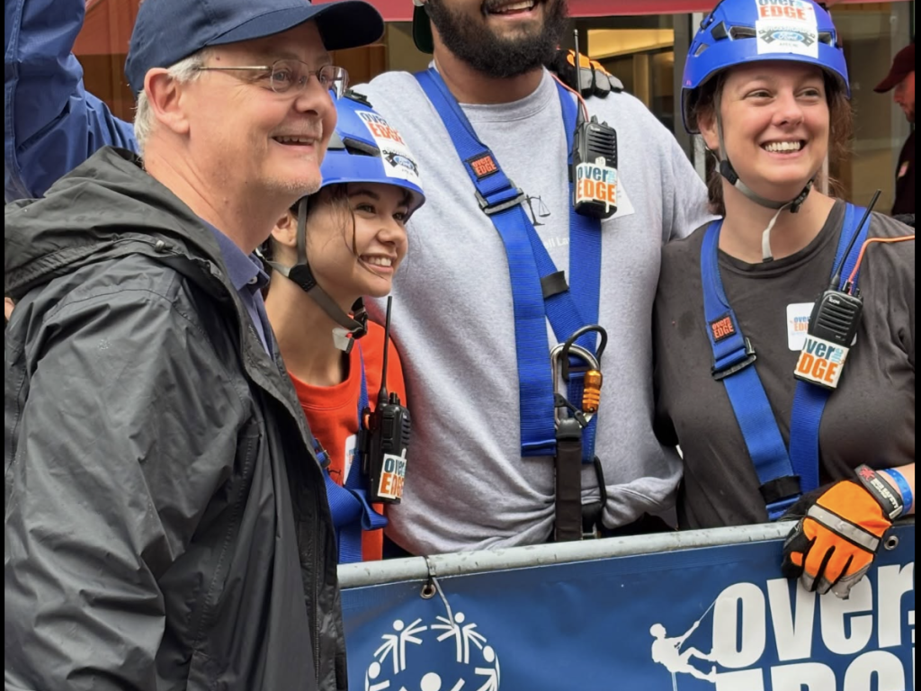 Photo of three Campbell Law students dressed in harnesses with a man from Special Olympics ready to go 'Over the Edge' for Special Olympics in 2025