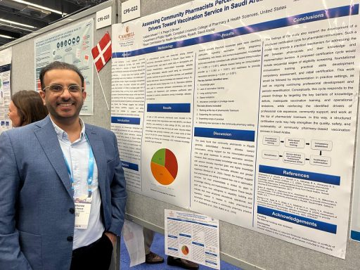 Man in blue suit coat and dark pants wearing lanyard standing in front of research poster