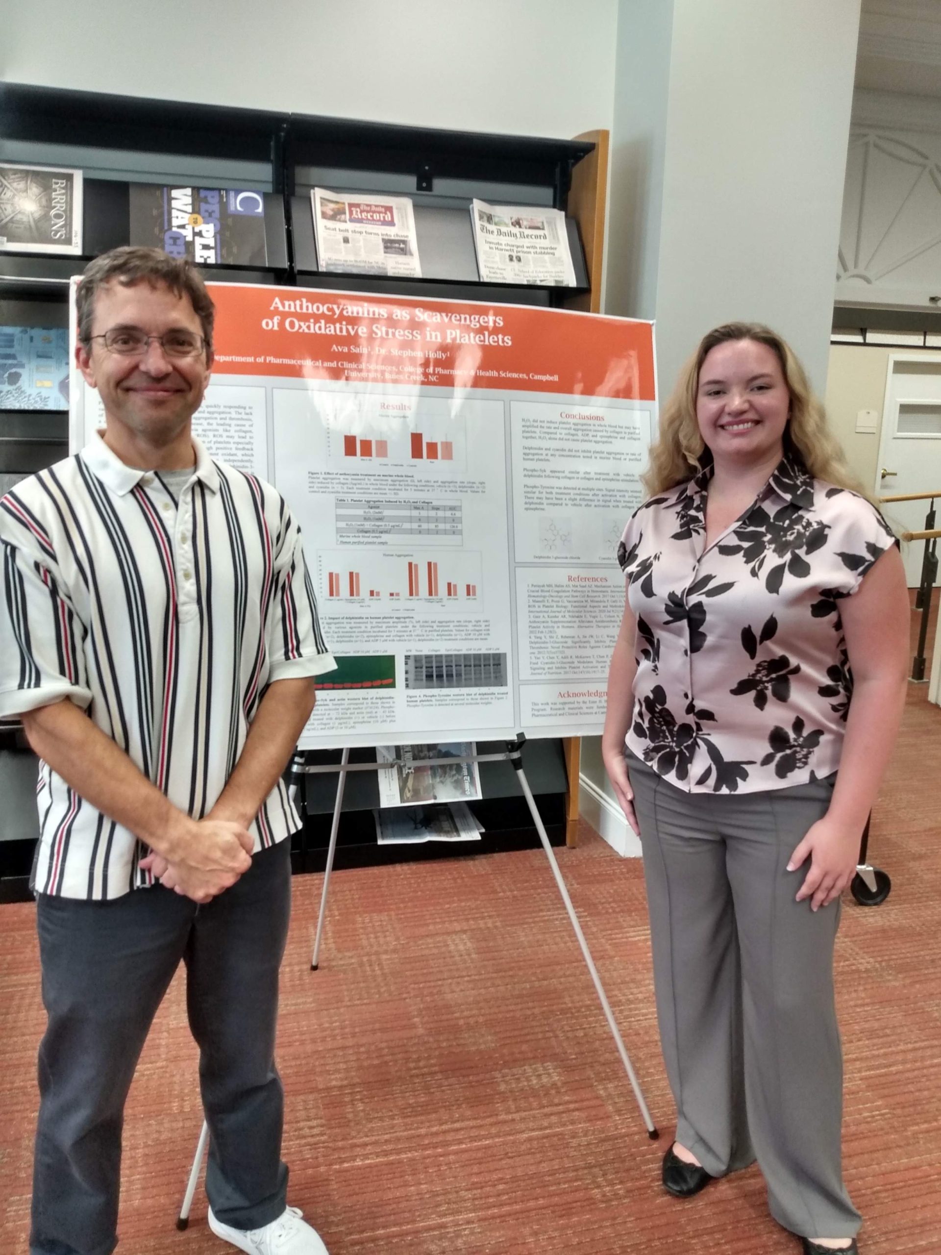 Faculty member and student standing on each side of a research poster
