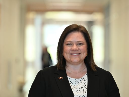 Female in business suit standing in a hallway smiling at the camera.