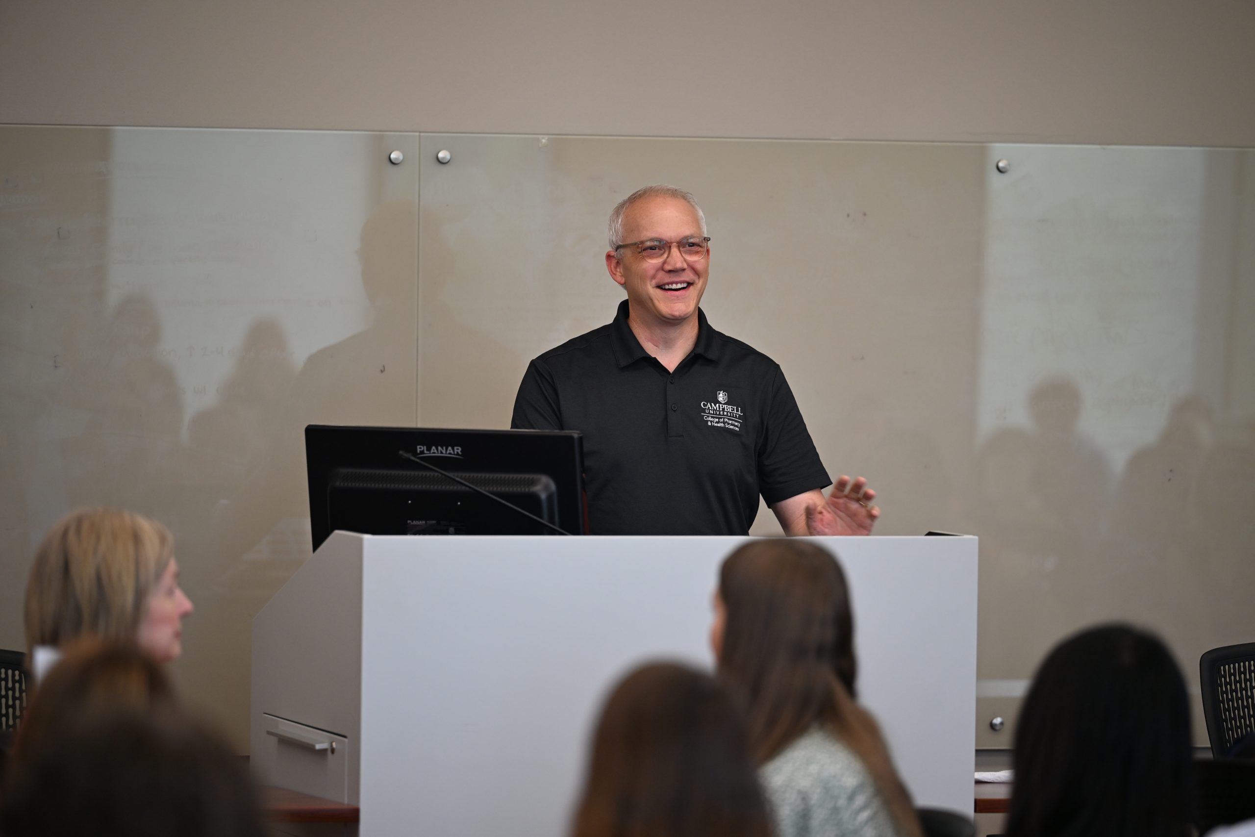 Man wearing dark polo shirt standing a podium 
