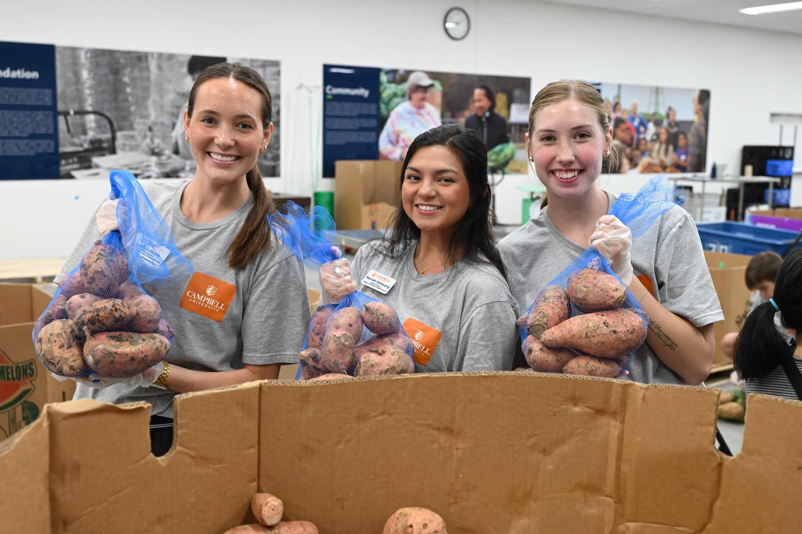Three students holding bags of potatoes they packed.