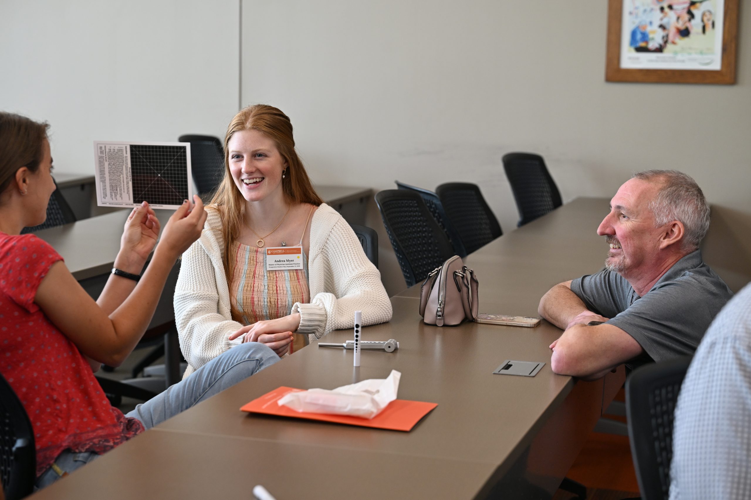 Faculty member squatting down at a table helping two students with an eye exam
