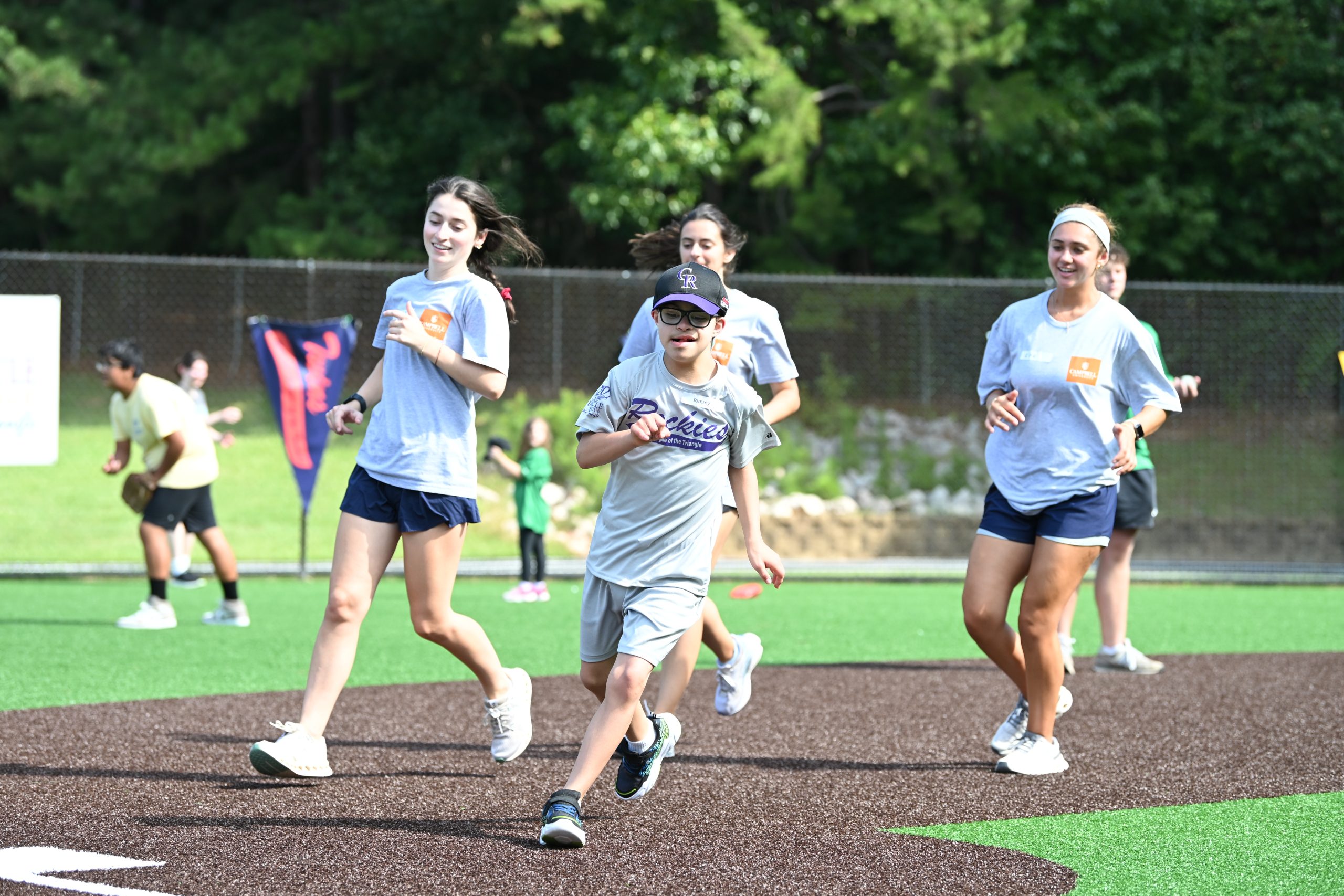 Students running the bases with an athlete at the miracle league game.