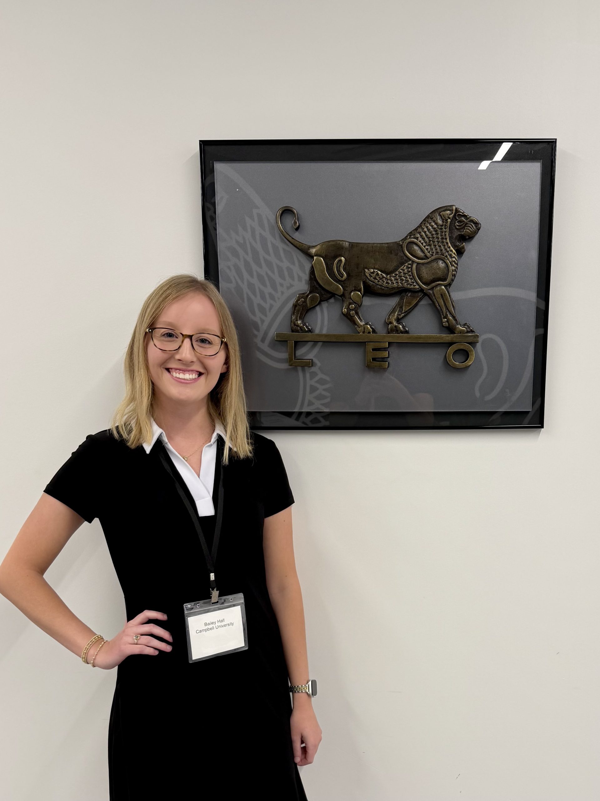Female student wearing black dress with white collar stands with hand on hip in front of wall art of a lion.