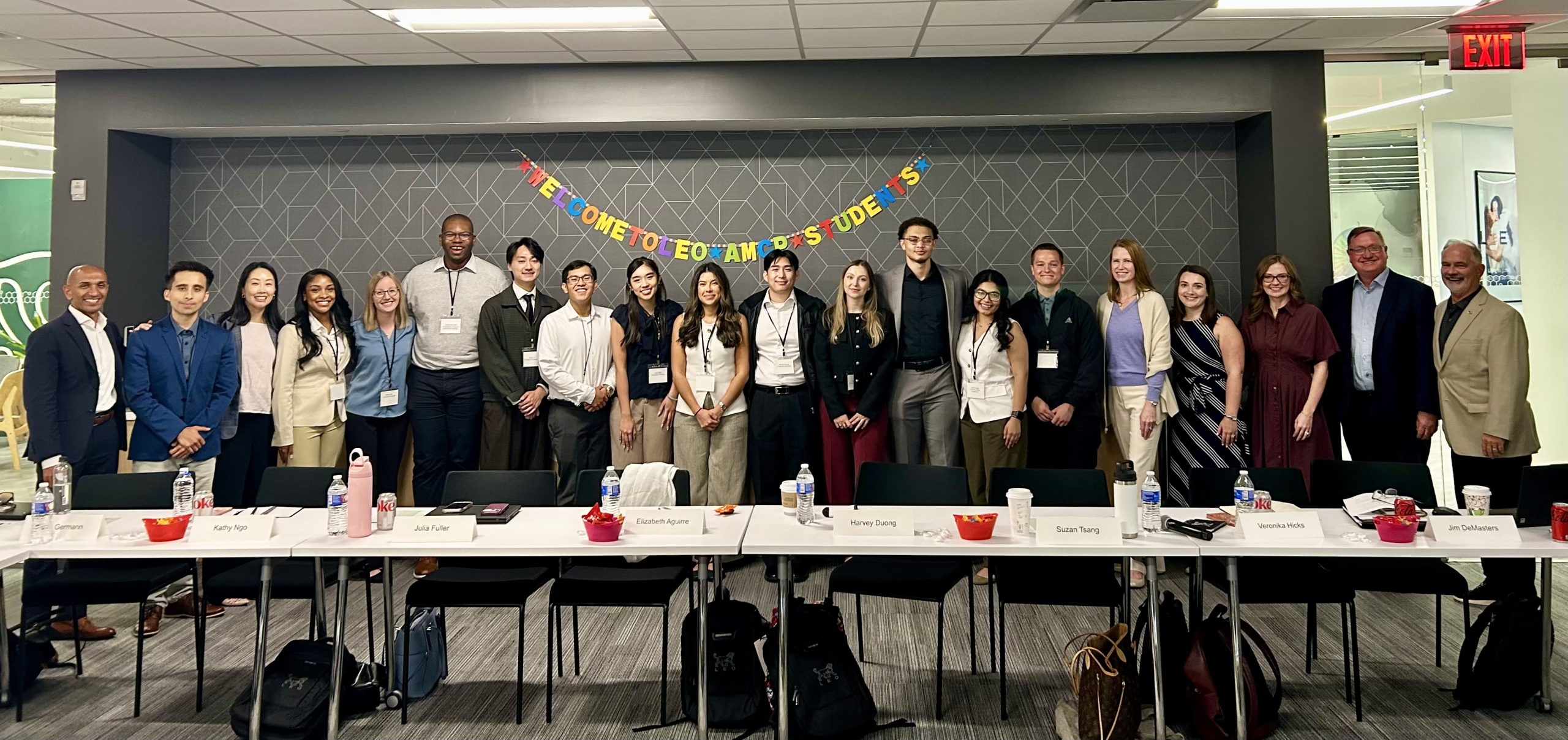 Group of pharmacy students and executives standing in a row with a welcome banner behind them.