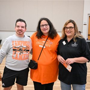 Three attendees wearing Campbell apparel smile together for a photo at the Alumni Block Party.