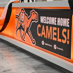 An orange and black banner featuring Campbell’s camel logo reads “Welcome Home Camels!”
