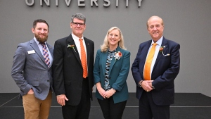 Three 2026 Distinguished Alumni honorees wearing orange floral pins pose with Alumni Board President Morgan Timiney at the Distinguished Alumni Dinner.