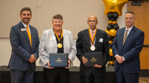 Two Golden Club inductees wear gold medallions and hold Campbell University certificate folders while posing with Director of Planned Giving, Grant Harden and University President Dr. William M. Downs at the 2026 induction luncheon.