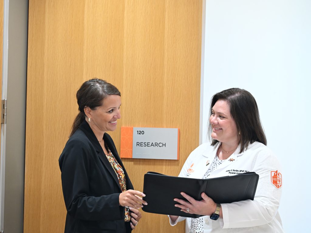 Woman in dark suit holding a padfolio with a woman in a white coat